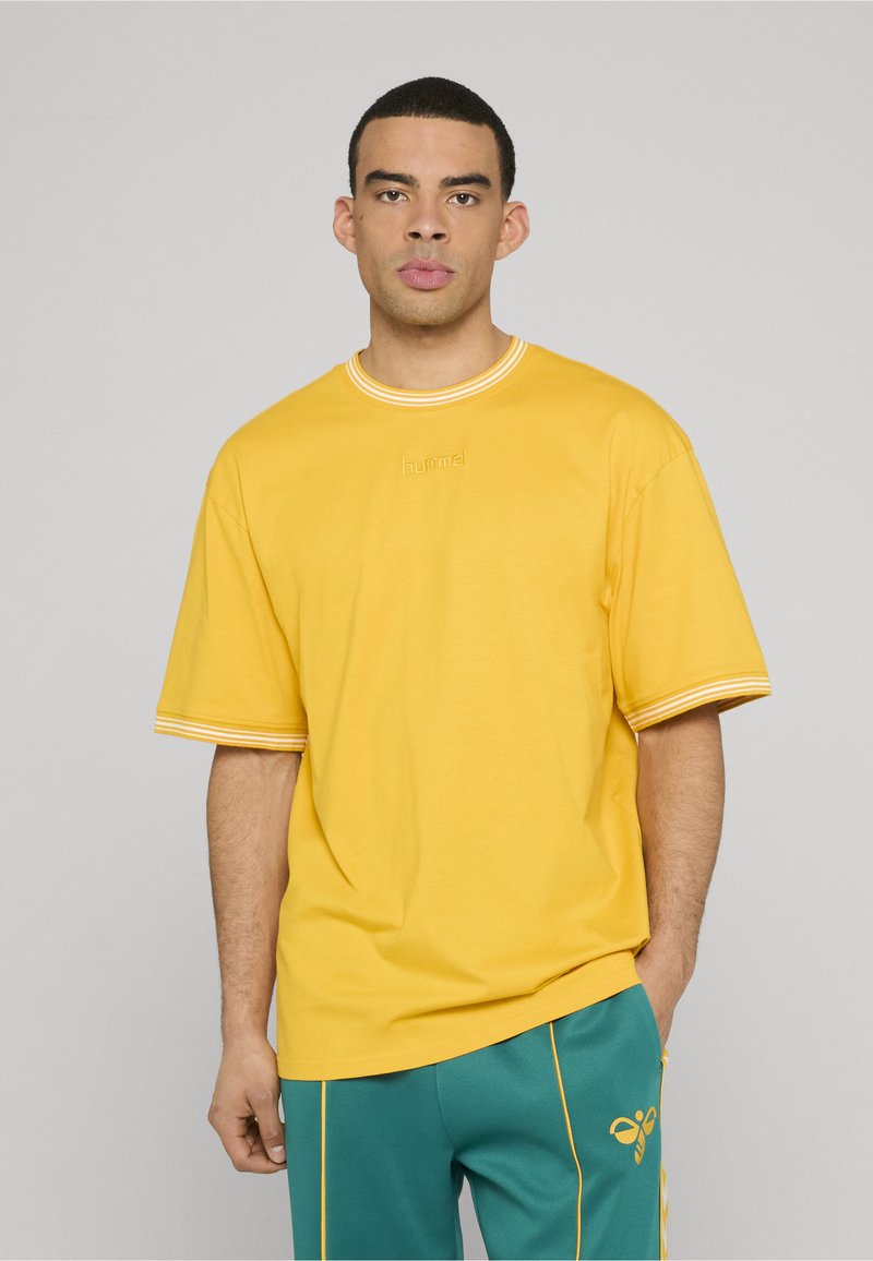 T-shirt en coton jaune à manches courtes, avec un col côtelé et des accents rayés sur les manches. Logo brodé au centre de la poitrine.