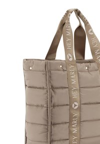 Sac fourre-tout rembourré en taupe clair avec une texture cousue verticalement. Il dispose de deux poignées en tissu avec le logo "HEY MARLY" en beige d'un côté.