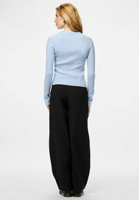 Gaiši zils ribots adīts džemperis ar pieguļošu siluetu, valkāts ar augstā jostasvietā melniem platā šortiem, uzsverot gludu tekstūru.