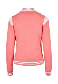 Sweat-shirt corail avec des accents blancs sur les épaules, un col et des poignets côtelés, et deux rayures blanches à la taille, fabriqué dans un matériau doux.