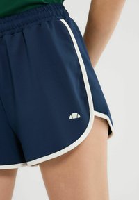 Marineblauwe sportbroek met witte zijkanten en een klein logo aan de voorkant. Gemaakt van lichte, soepele stof met een elastische tailleband.