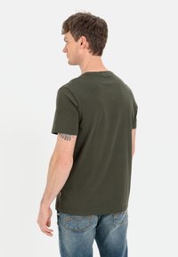 Olivengrønt bomulds T-shirt med korte ærmer, rund hals og lige pasform. Har et lille mærke på siden og er parret med blå denim jeans.
