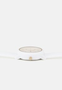 Reloj de silicona blanco con una esfera beige redonda, marcadores de hora en tono dorado y una corona lateral para ajustar la hora.