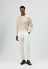 Beige geribbelde trui gecombineerd met op maat gemaakte witte broek en donkerbruine loafers; gladde textuur en strakke lijnen benadrukken een minimalistisch ontwerp.