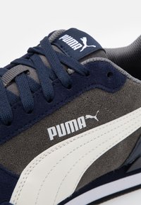 Baskets en daim bleu marine et gris avec logo Puma en cuir blanc, lacets plats et accents en tissu texturé. Conçues pour un usage athlétique.