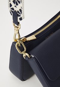 Sac en cuir navy avec une finition texturée, doté d'une fermeture éclair et de quincaillerie dorées, ainsi que d'une sangle en tissu à motif.