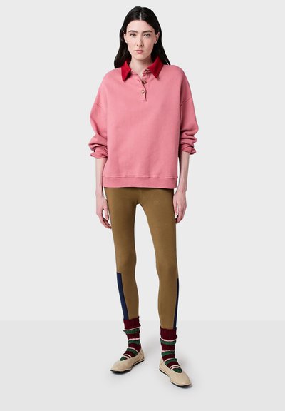 Pink oversized sweatshirt with a red collar and three buttons, paired with brown leggings featuring navy accents and striped socks.