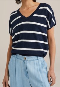 Marinblå randig kortärmad V-ringad topp i mjukt material, med vita horisontella ränder och avslappnad passform, tillsammans med ljusblå veckade byxor.