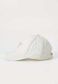 Valkoinen puuvillainen baseball-lakki, jossa on vaaleanpunainen brodeerattu logo, kaareva lippa, kuusiosainen muotoilu ja säädettävä hihna takana.