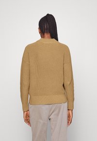 Maglione marrone a maglia con una texture a coste, vestibilità comoda e scollatura a girocollo, con spalle cadenti e orlo leggermente accorciato.