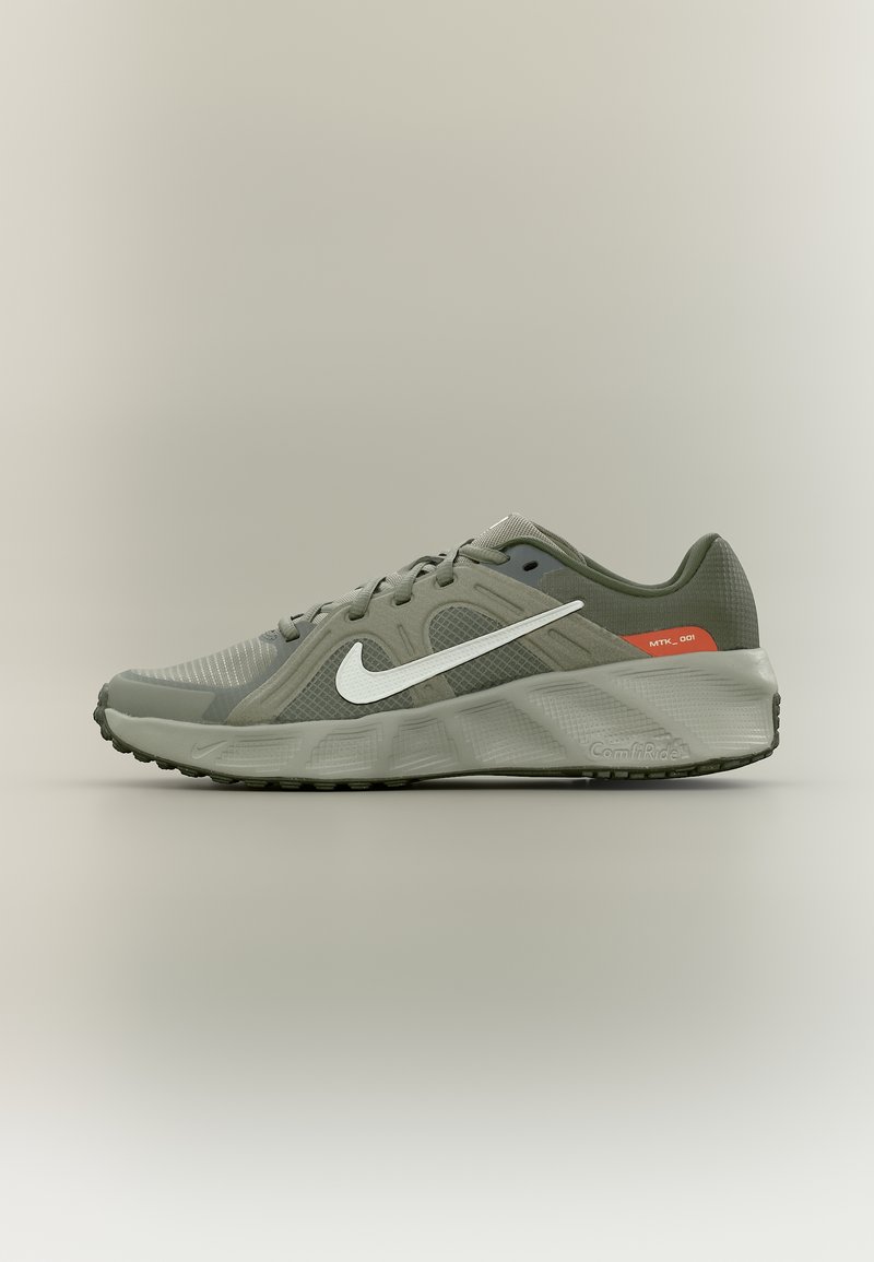 Γκρι παπούτσι τρεξίματος Nike με λευκή σήμανση Swoosh, επάνω μέρος από δίχτυ και συνθετικό υλικό, μαλακή σόλα και μικρή κόκκινη λεπτομέρεια κοντά στη φτέρνα σε ουδέτερο φόντο.