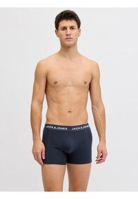 Νέος άντρας που στέκεται μπροστά σε απλό φόντο φορώντας σκούρα μπλε εσώρουχα boxer της Jack & Jones, κοιτάζοντας προς τα εμπρός με ουδέτερη έκφραση.
