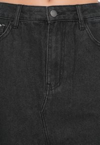 Pantalonii din denim negri au talie înaltă, închidere cu nasture în față și ușoară uzură în zona buzunarului stâng. Material texturat și croială clasică.
