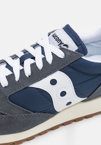 Sport shoes featuring navy blue nylon and grey suede, white accents, and contrasting rubber outsole. White laces and brand logo visible.