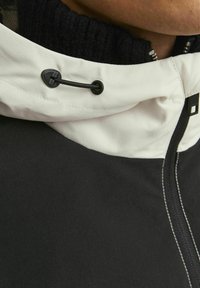 Giacca nera con colletto bianco, collo elasticizzato, cordino regolabile e zip laterale con dettagli di cucitura a contrasto.