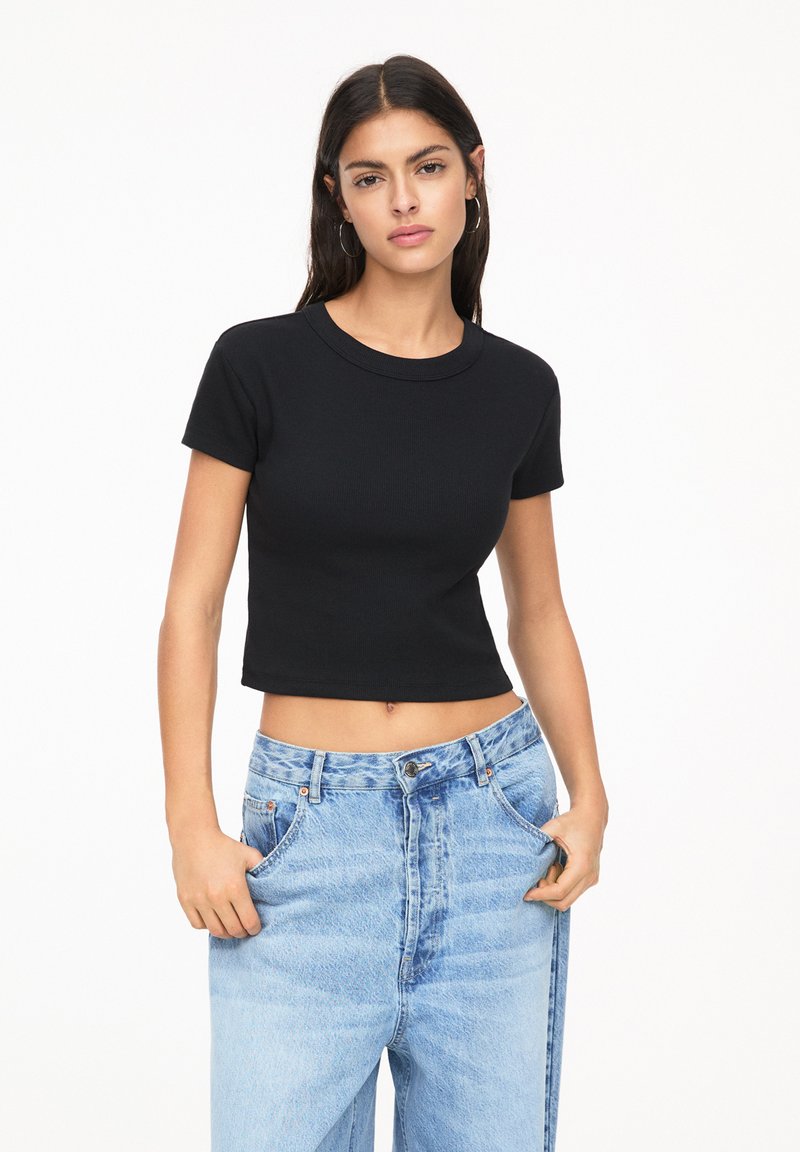 Zwart cropped t-shirt met korte mouwen en een ronde halslijn, gemaakt van ribstof. Gecombineerd met lichtblauwe, high-waisted denim jeans.