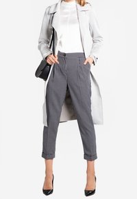 Light gray trench coat over a white satin blouse, paired with black and white checkered cropped trousers and black high heels.