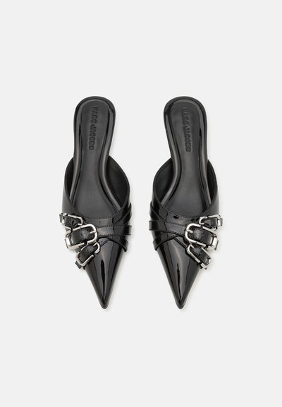 Mules de charol negro con puntas afiladas, acentos de doble hebilla y un diseño de espalda abierta. Textura suave con un acabado brillante.