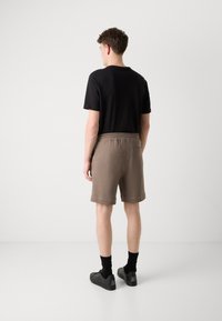 T-shirt noir, shorts marron avec une taille élastique et baskets noires. Les shorts ont une poche arrière et une texture lisse.