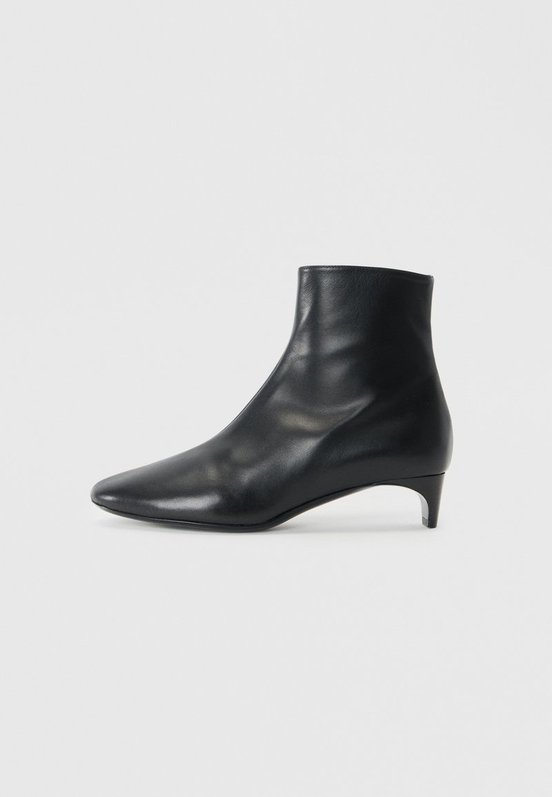 Bottine en cuir noir avec un bout pointu et un talon courbé de hauteur moyenne. Texture lisse et design sans couture sans matériel visible.
