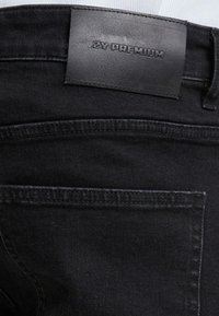Jeans de mezclilla negra con una etiqueta de cintura de cuero texturizado estampada con "2Y PREMIUM". Incluye bolsillos traseros con costuras cosidas.