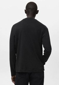 Črna majica s tekstom z dolgimi rokavi iz bombaža. Ima zaobljen vratni izrez, sproščen kroj in preprost dizajn z gladko teksturo ter minimalnim oblikovanjem.