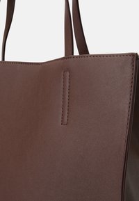 Brązowa skórzana torba klasyczna o gładkiej teksturze, z wydłużonymi uchwytami i górnym przeszyciem wzdłuż krawędzi. Minimalistyczny design, bez widocznych elementów metalowych.