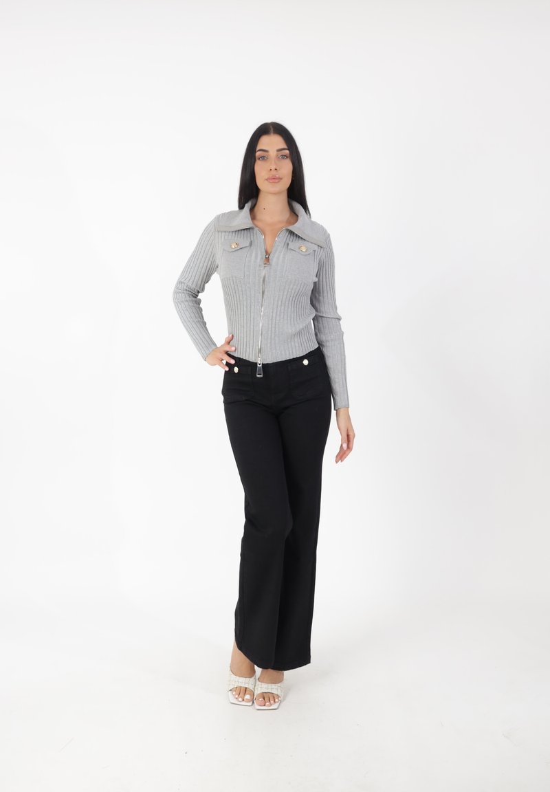 Top gris de crepé con cremallera y cuello, con dos bolsillos en el pecho, combinado con pantalones negros de pierna ancha y calzado de abierta con adornos.