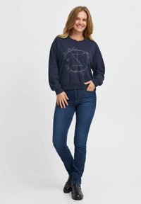 Sudadera azul marino con bordado floral, cuello redondo y mangas largas. Combinada con jeans de mezclilla oscuros y botines negros.
