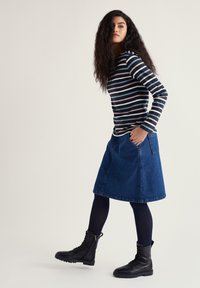 Csíkos hosszú ujjú blúz sötétkék, zöld és rózsaszín színekben; kék farmer A-vonalú szoknya; bordázott sötétkék harisnya; fekete cipzáros bokacsizma.