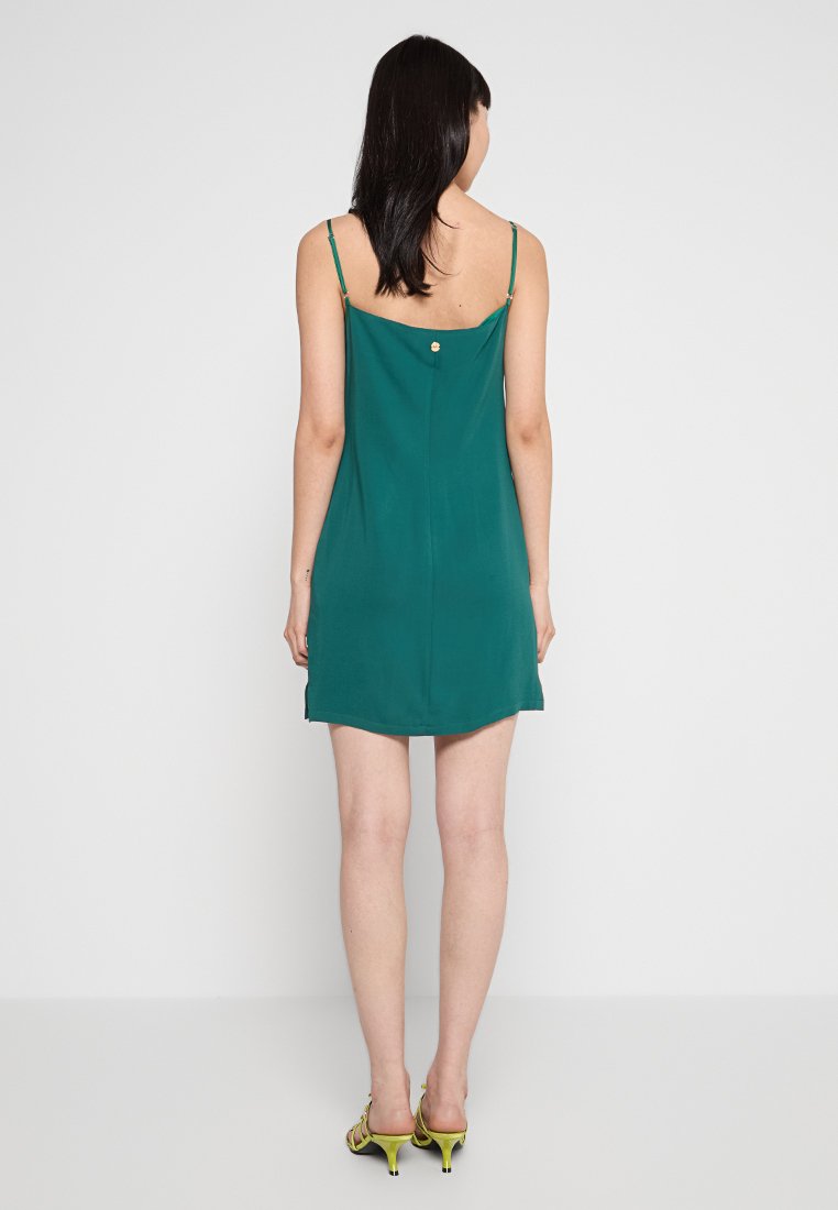 Ärmeloses grünes Kleid mit geradem Schnitt, dünnen Trägern und einer Knopfdetaillierung am Rücken. Glatte Textur und knielanges Design.