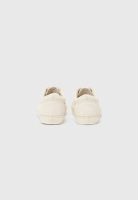 Off-white suede sneakers featuring a low-top design, round toe, and tonal laces. Heel tag displays logo; rubber sole for traction.