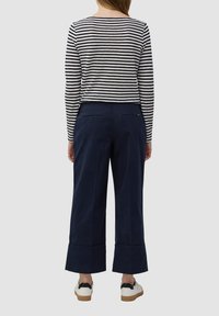 Maglietta a maniche lunghe a righe blu navy e bianca, abbinata a pantaloni ampi blu navy con tasche posteriori e lunghezza cropped, indossata con sneakers bianche.