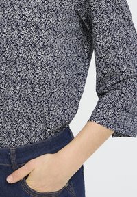 Navybluse med hvidt blomsterprint, letvægtsstof, trekvartlange ærmer og en afslappet pasform, kombineret med mørke denimjeans.