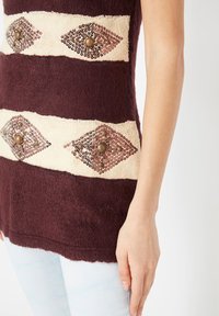 Top de punto con rayas en tonos burdeos y crema, adornado con patrones de diamantes de lentejuelas y botones decorativos. Textura suave, corte relajado.