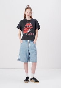 Black graphic t-shirt with red lips design, paired with light blue denim shorts featuring white side stripes; black sneakers with beige soles.
