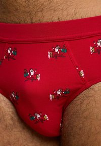 Czerwone bawełniane majtki z małymi motywami Świętego Mikołaja latającego samolotem z prezentami. Miękka faktura z elastycznym paskiem w talii.