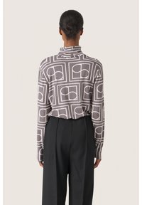 Hallx sleeves olematu blouse hallist kangast, millel on geomeetriline valge muster; kõrge kaelusega, millel on peene tekstuur, koos mustade kõrge vöökoha pükstega.