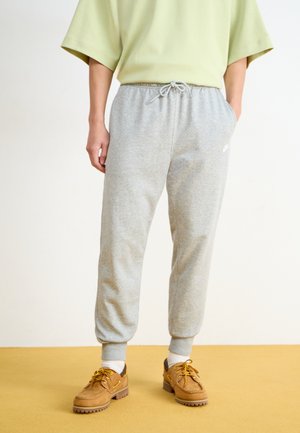Pantalons de survêtement gris en tissu doux avec une taille élastique et un cordon de serrage réglable. Associés à des chaussures marron et des chaussettes blanches.