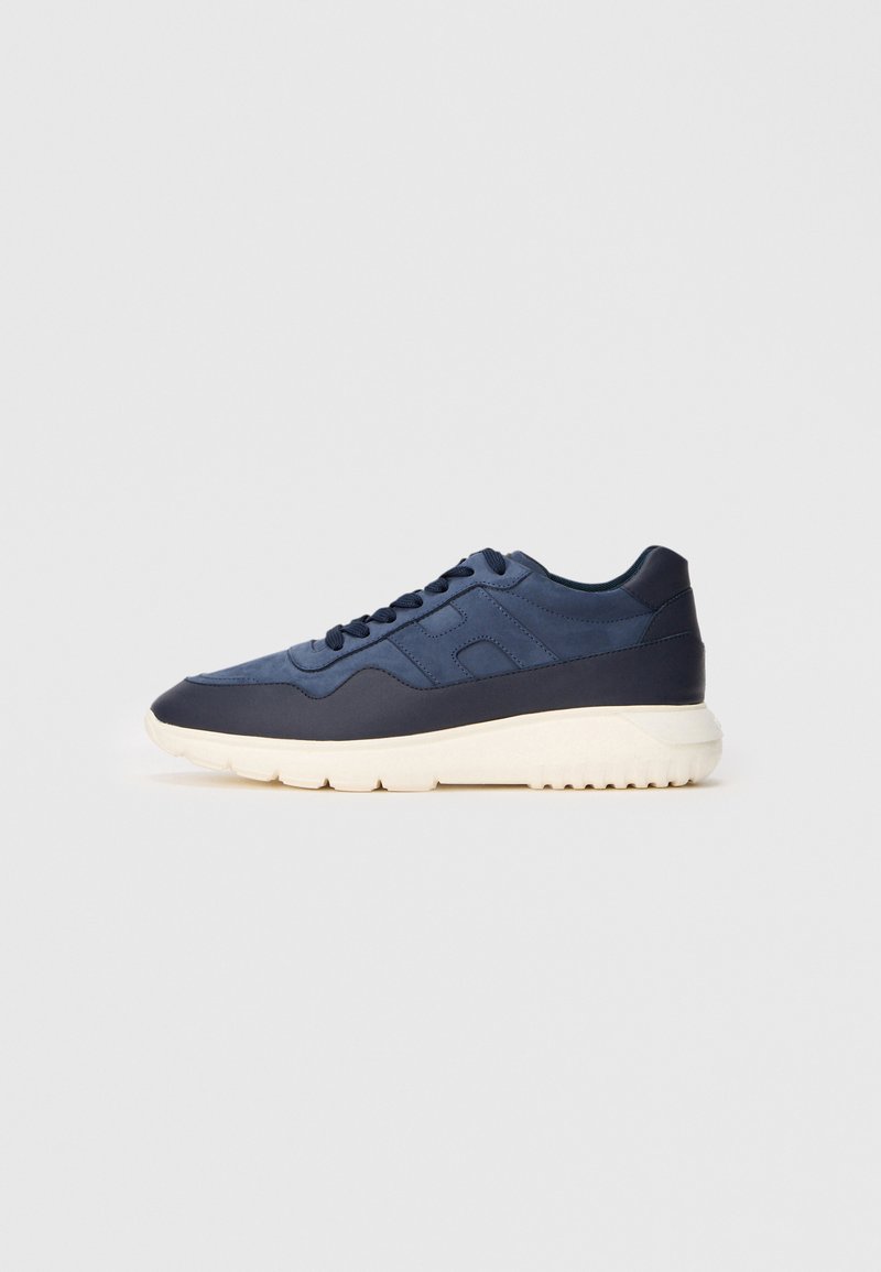 Baskets de sport bleu marine avec un dessus synthétique lisse, un système de laçage, et une semelle en caoutchouc blanc texturé. Accentué par des coutures subtiles.
