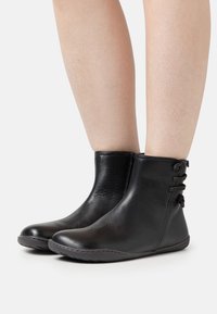 Black leather ankle boots with smooth texture, rounded toes, side lacing detail, and a flexible rubber sole.