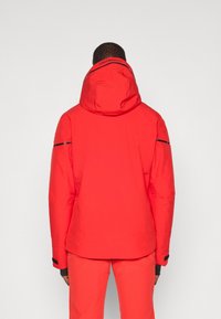 Rød isolert jakke med hette, med sorte detaljer og reflekterende elementer. Glatt tekstur, designet for varme og beskyttelse.