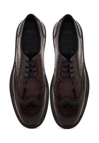 Zapatos de vestir de cuero pulido marrón con diseño de ala y detalles de brogue, y cordones negros. Textura suave y silueta curvada.