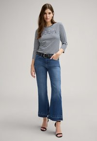 Camicetta a righe con maniche lunghe con testo, jeans blu a zampa d'elefante con orlo grezzo, cintura nera e tacchi aperti neri. Design semplice e vestibilità casual.