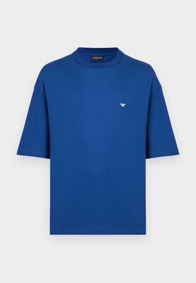 Μπλουζάκι σε βασιλικό μπλε χρώμα με κοντά μανίκια, κατασκευασμένο από βαμβάκι, με στρογγυλή λαιμόκοψη και μικρό λευκό λογότυπο αετού στο αριστερό στήθος.