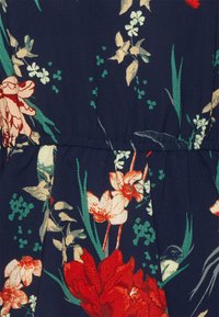 Vestido floral com fundo azul-marinho, flores vermelhas e bege, folhas verdes e uma cintura franzida para forma e textura.