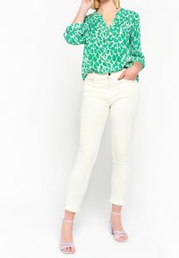 Grön leopardmönstrad blus ihop med vita, slim-fit byxor och lila remsandaler med klack. Har en v-ringning och knapprad på skjortan.