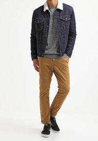 Ciemnoniebieska jeansowa kurtka z białym kołnierzem z sztucznego owczego futra, noszona na szarym swetrze, w połączeniu z beżowymi chinosami i czarnymi sneakersami.