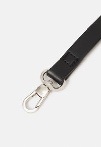 Sangle en cuir noir avec des accessoires en métal argenté, présentant un détail rectangulaire cousu et un clip pour une fixation sécurisée.