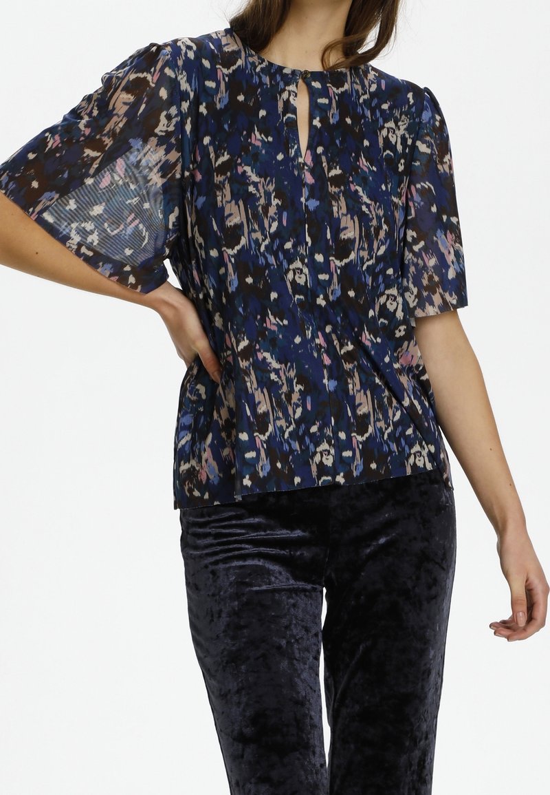 Lehký modrý blouse s různorodým vzorem v odstínech hnědé, růžové a modré. Obsahuje krátké nabírané rukávy a výstřih s klíčovou dírkou a detaily na knoflík.